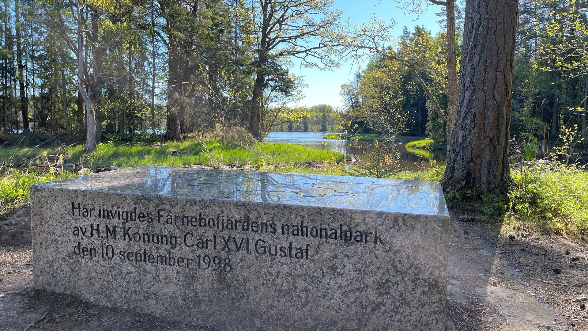 Minnessten vid Färnebofjärdens nationalpark intill vattendrag, omgiven av löv- och barrskog. Stenen markerar invigningen av nationalparken 1998.