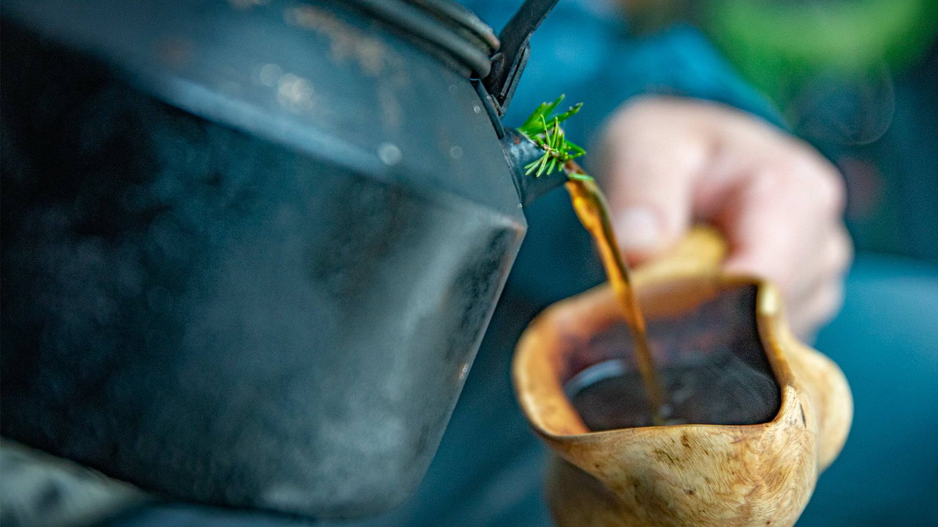 Foto av en kaffekanna som häller kaffe i en träkåsa.