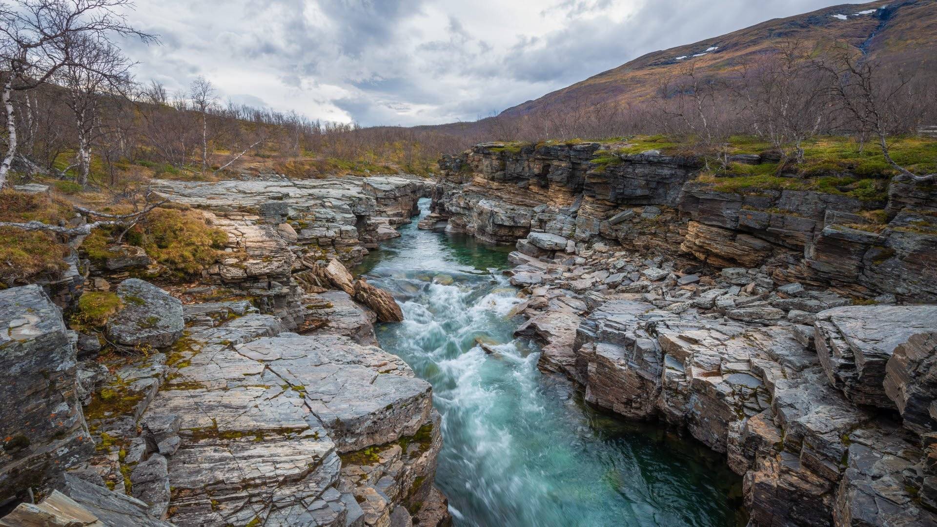 Abiskojåkka slingrar sig genom en smal, stenig ravin omgiven av kala fjäll och klippor. Abisko, Lappland, Sverige.