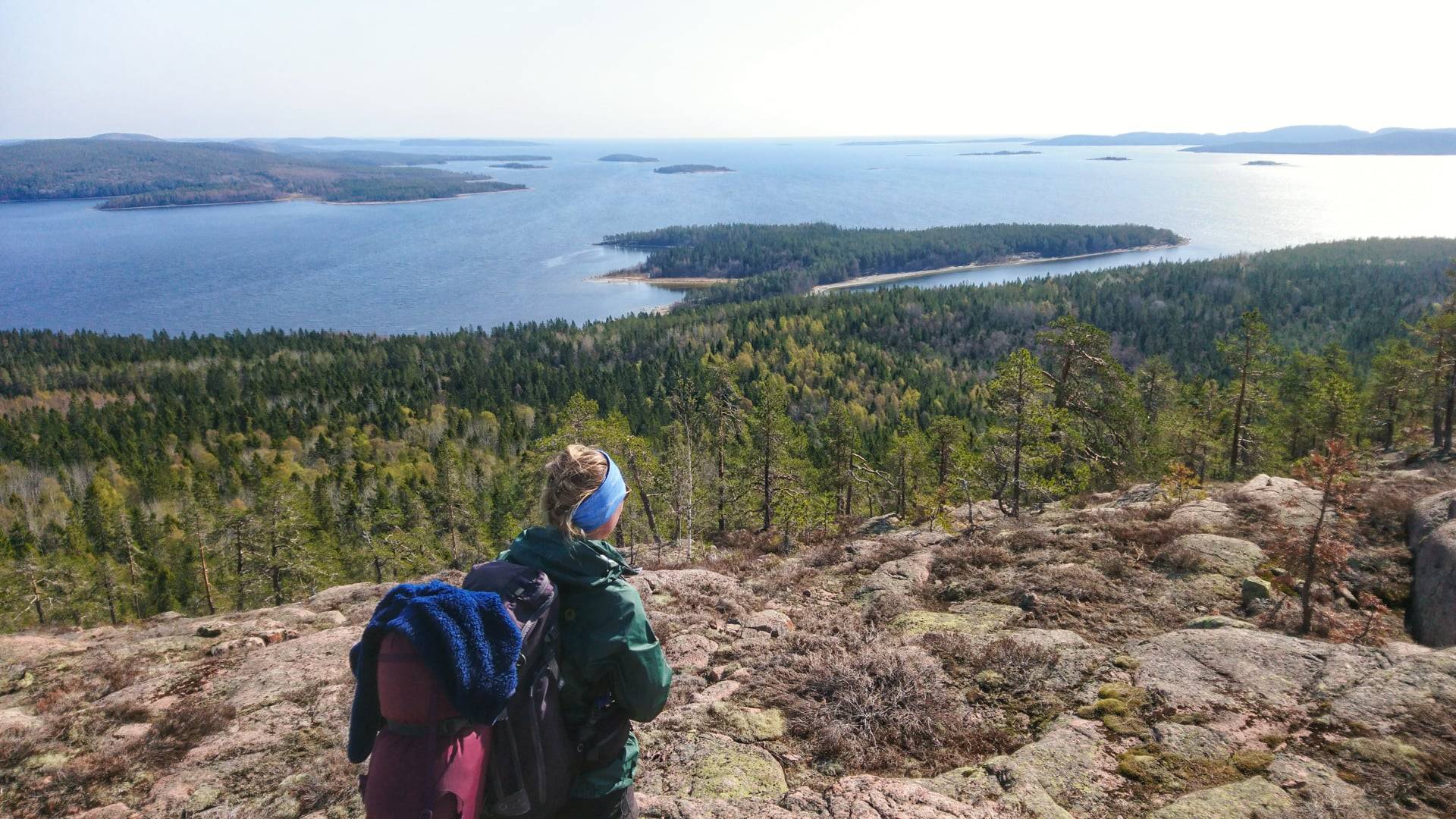 Foto av en person med vandringsryggsäck som står på en höjd framför en utsikt mot havet.
