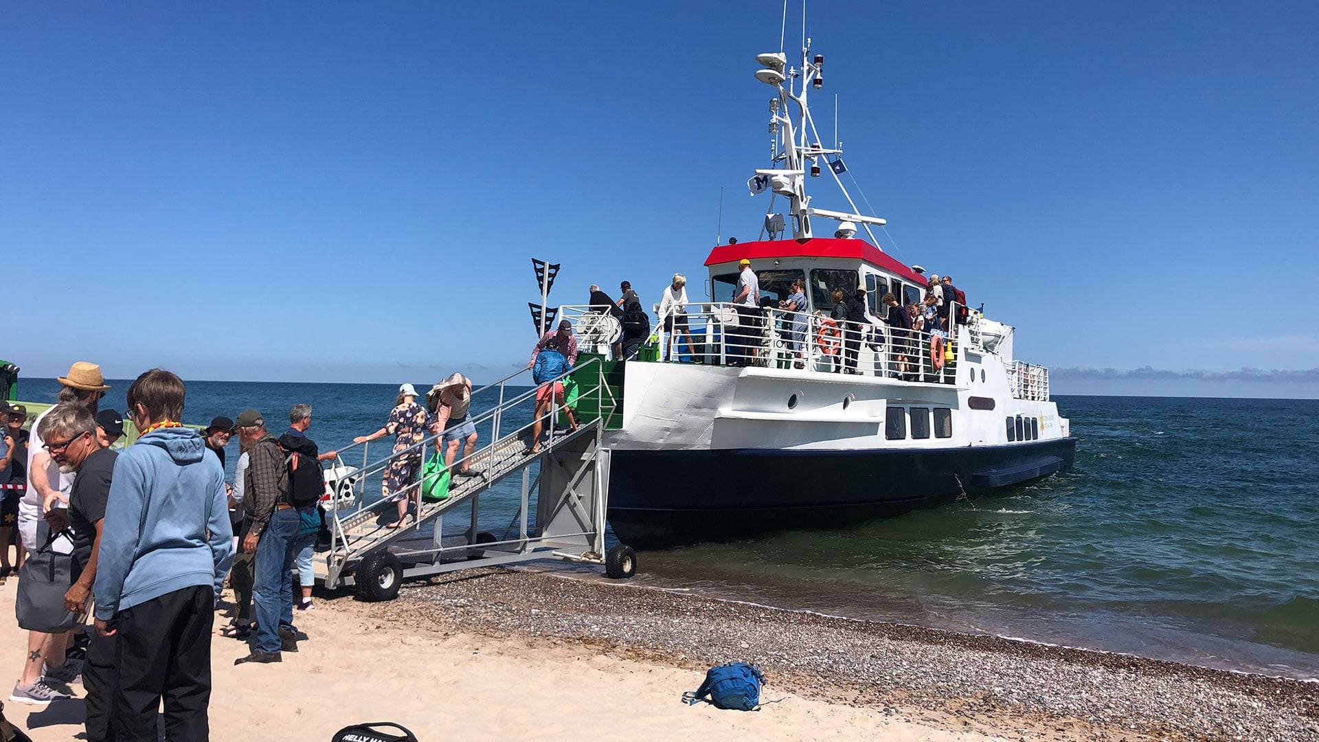 Färja vid sandstrand med människor på landgången.