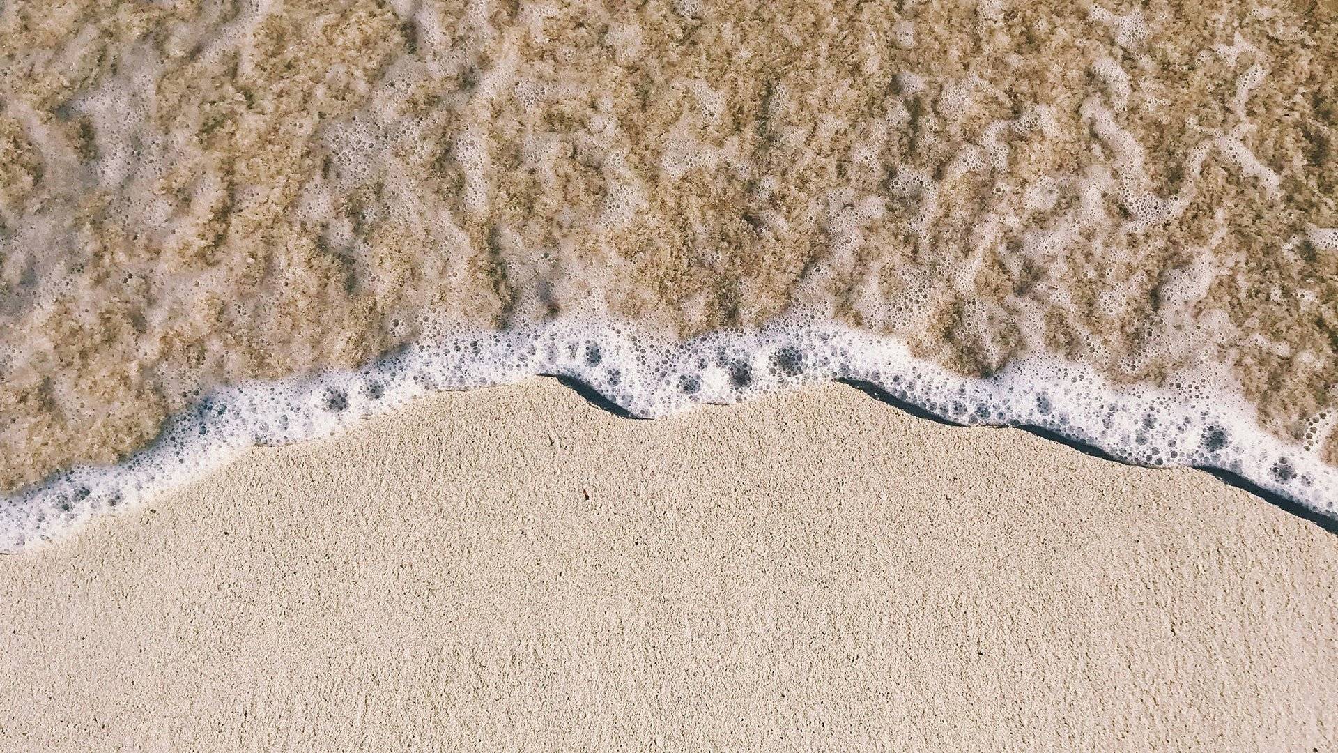 Vågskum rullar in över en slät sandstrand.