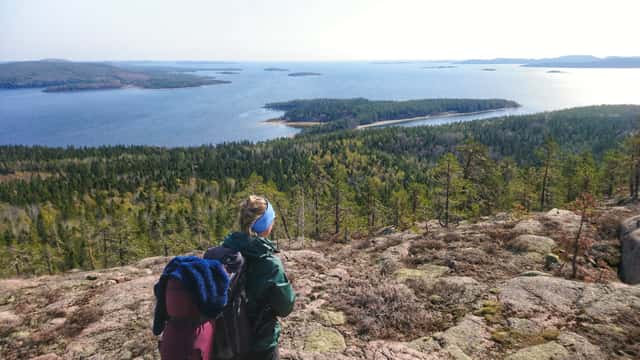 Foto av en person med vandringsryggsäck som står på en höjd framför en utsikt mot havet.