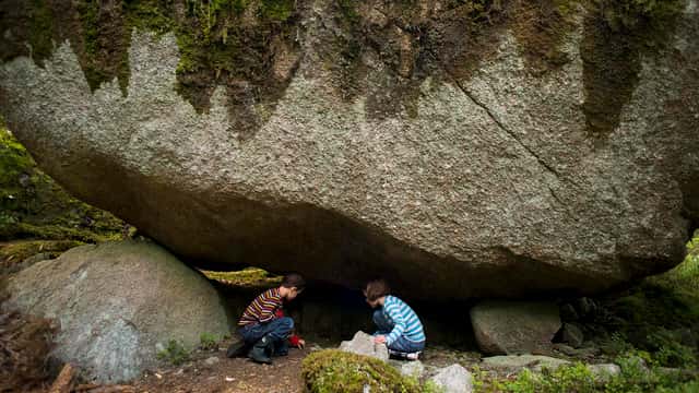 Två barn leker under stort stenblock