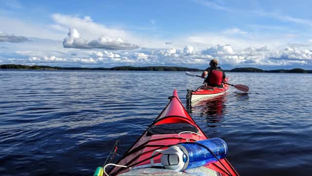 Två kanotister paddlar i sjön en solig dag, söder om Sandön i Färebofjärdens nationalpark.