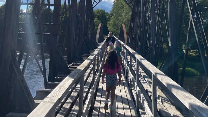 Jessica Berg Personer går över en träbro med räcken ovanför ett vattendrag i lummig grönska i Färnebofjärdens nationalpark.