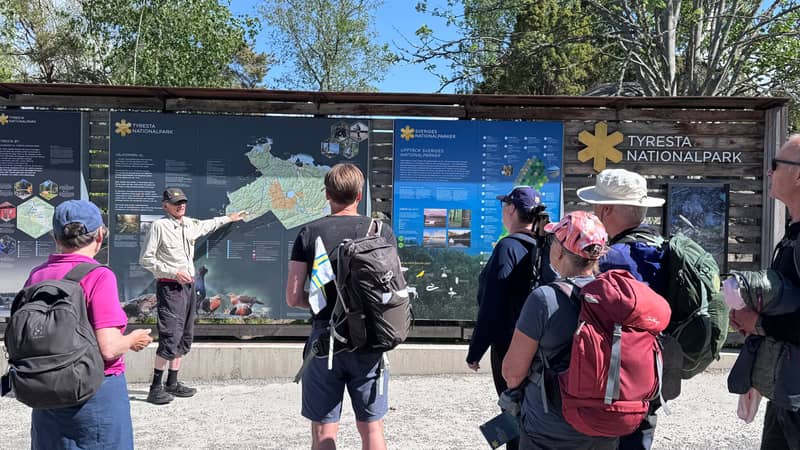 Tyresta nationalpark Flera personer med ryggsäckar står framför en informationsskylt i Tyresta nationalpark och lyssnar på en guide som pekar på kartan och berättar om nationalparken.