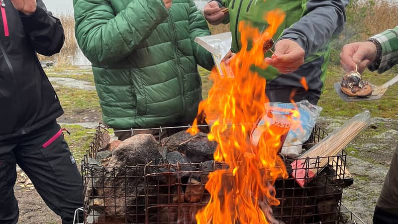 Personer samlade runt en öppen eld där mat tillagas över grillgaller.