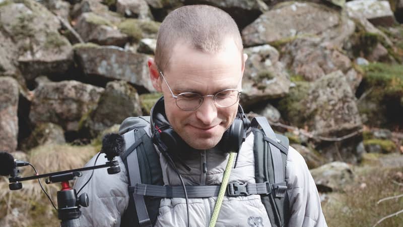Person med ryggsäck och hörlurar framför ett stenigt landskap.