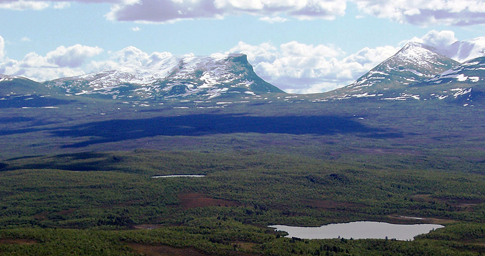 Lapporten, a U-shaped mountain valley on the horizon, in front of a lush mountain valley.