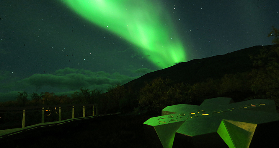 Skimrande grönt norrsken över mörk himmel.