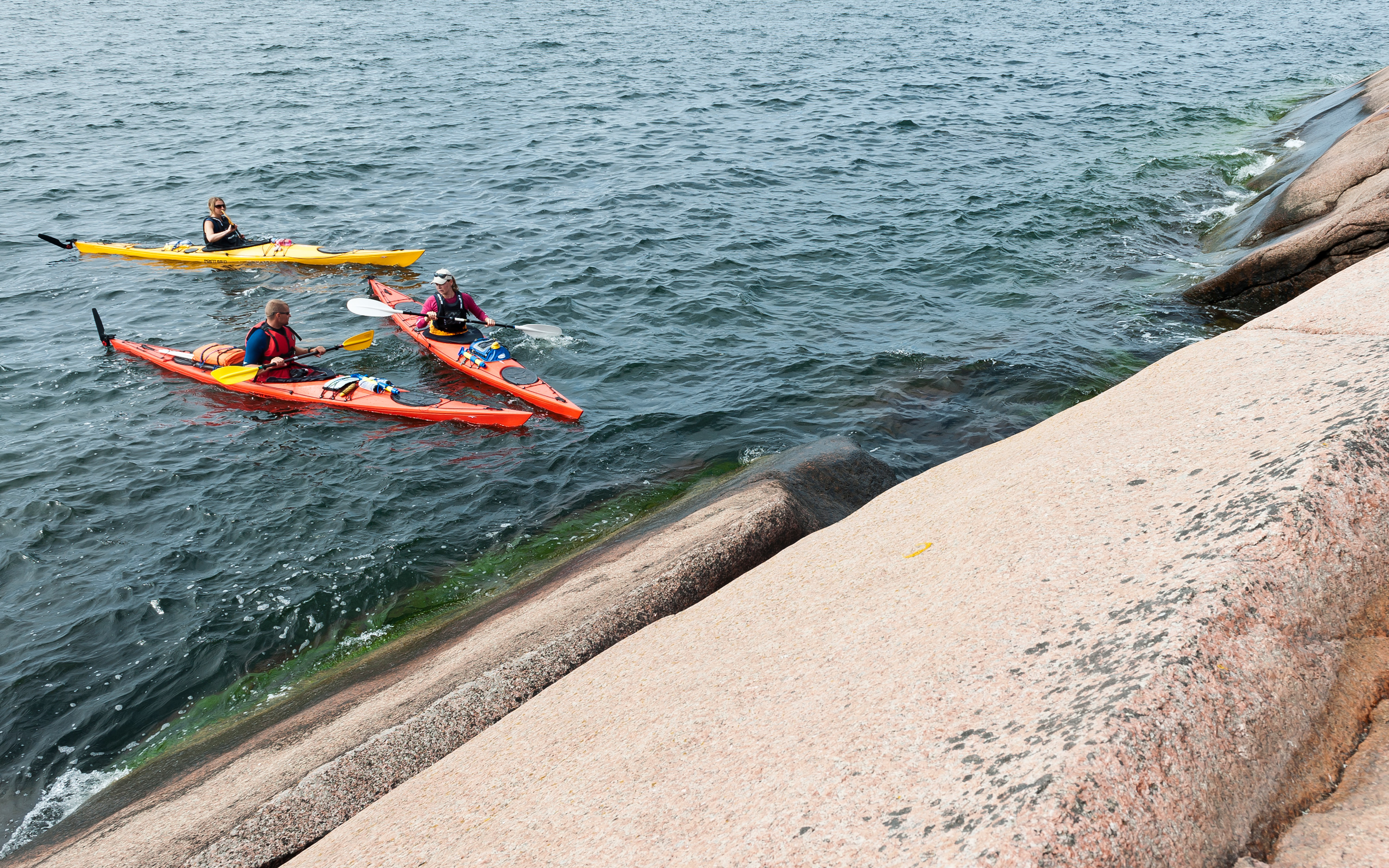 Tre personer i kajaker nära Blå Jungfruns klippor