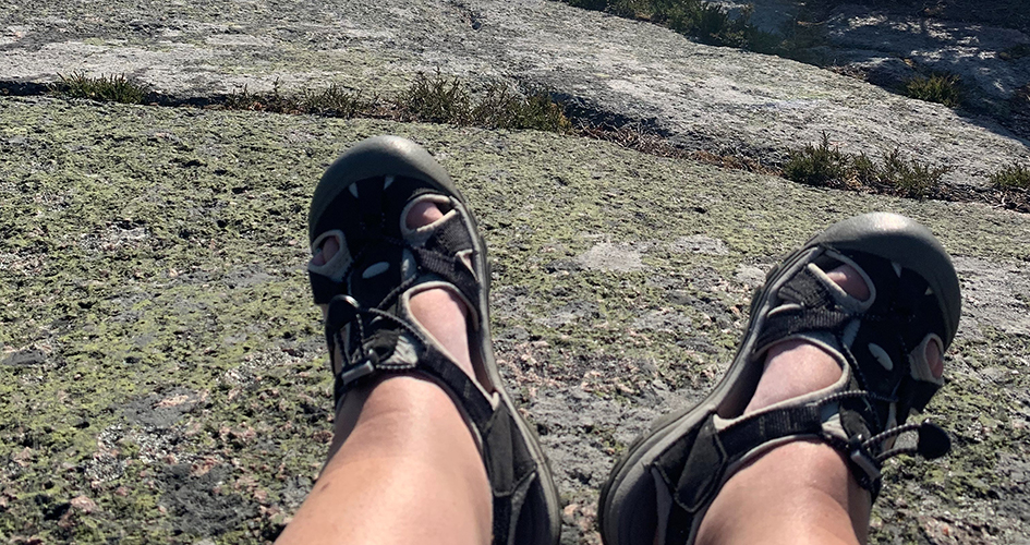 Ett par fötter i vandringssandaler som vilar på klippan.