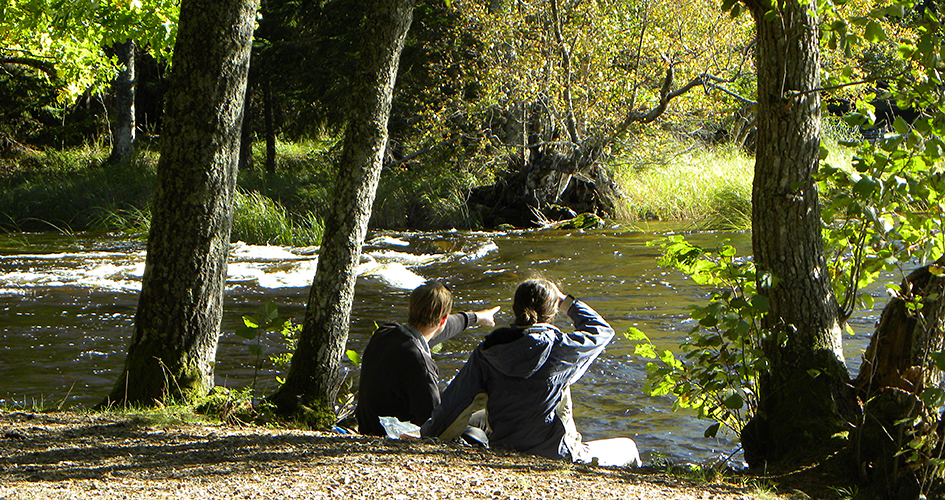 Två personer sitter vid kanten av älven och tittar på vattnet.