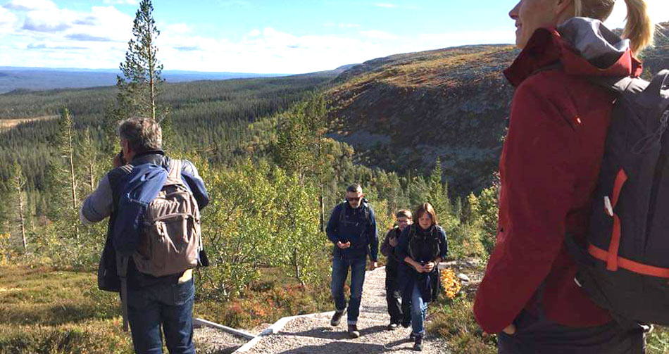 A group of people hike up a hill with magnificent scenery behind.