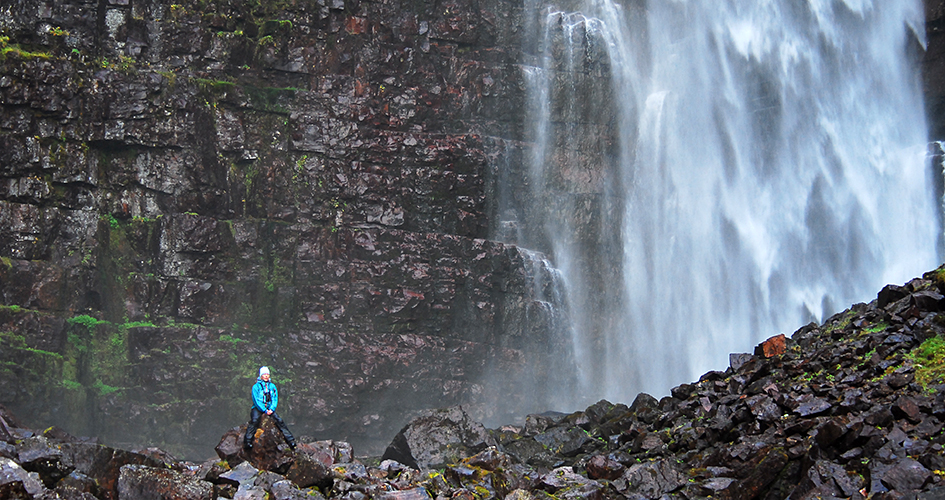 En person sitter på en sten framför vattenfallet njupeskär. 