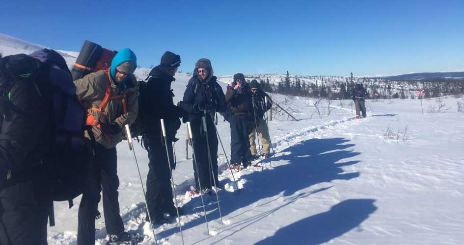 En grupp människor står med snöskor på led i snölandskap. 