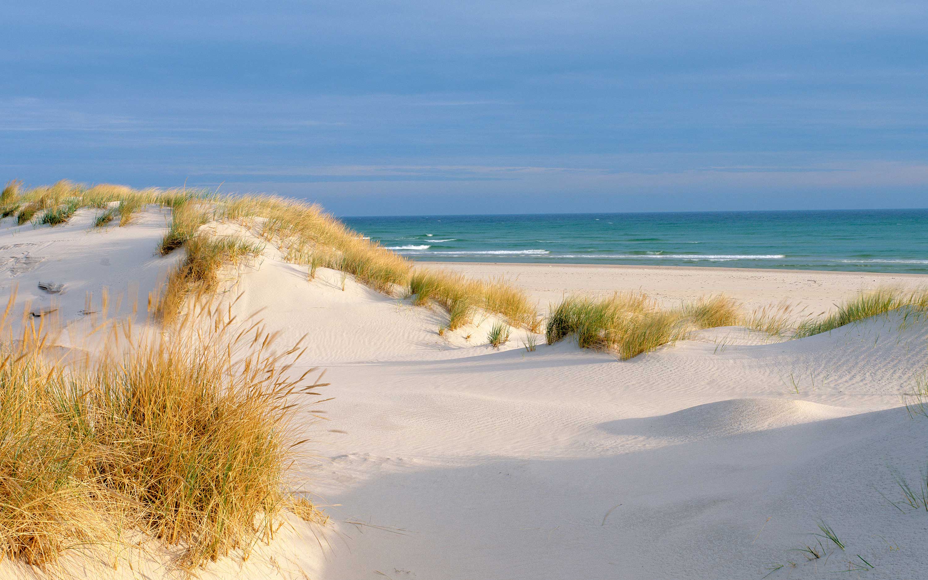 Sand dunes in front of blue sky and sea.