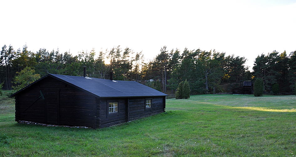 Low cabin in dark wood on open grass area.
