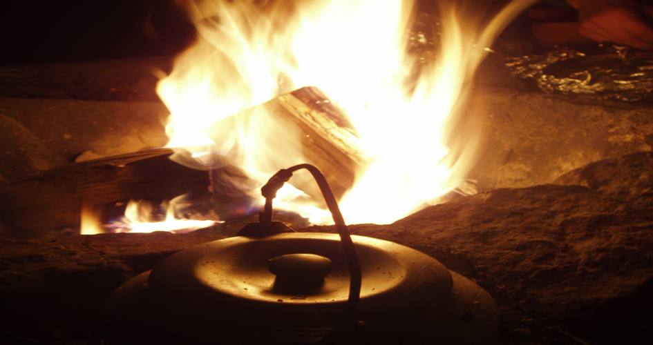 Kaffekittel framför en sprakande eld i mörkret.