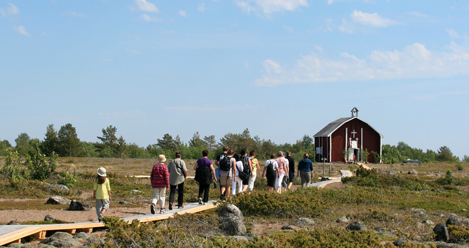 En grupp människor går på träspång på väg till röd träkyrka.