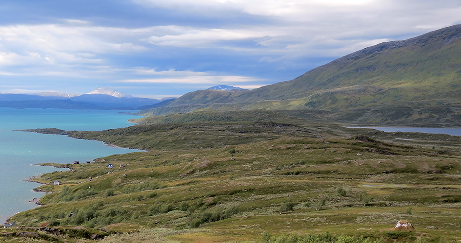 Fjällandskap med små hus vid standen av sjön Virihávrre, Padjelanta Badjelannda nationalpark, och fjällen i bakgrunden.