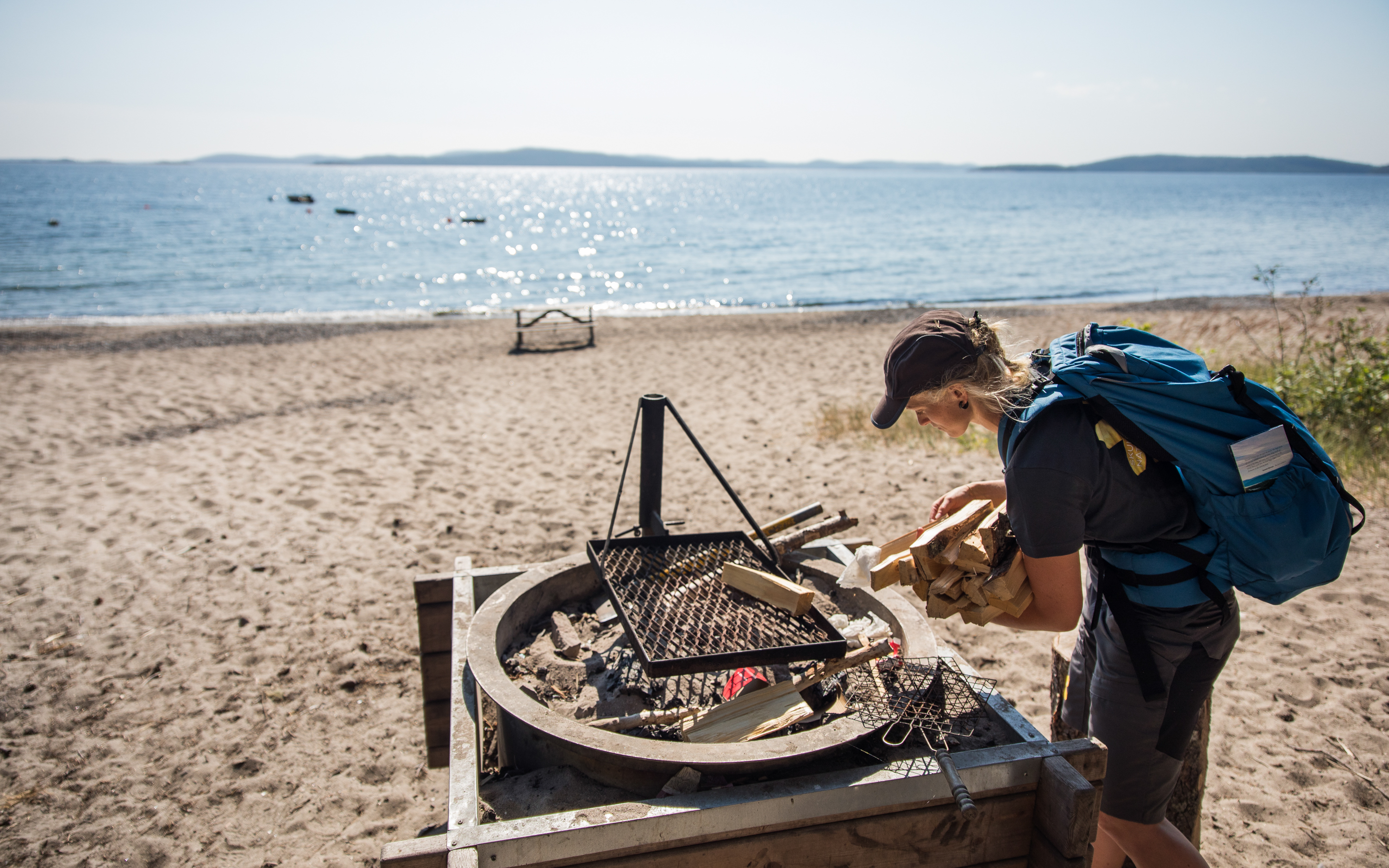 A girl holding fire wood at a fire place at a beach.