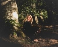 En kvinna sitter vid foten av ett bokträd. Solen lyser i ansiktet