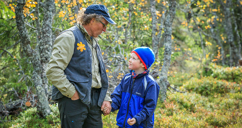 En av parkpersonalen pratar med ett barn omgiven av skog i höstskrud.