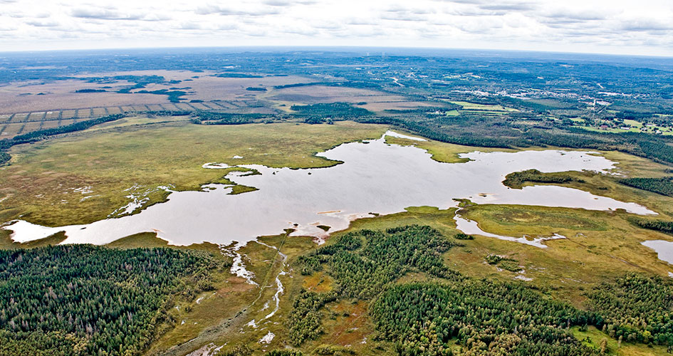 Flygbild över mossen med en sjö i mitten som speglar sig i blekgrått mot himlen.