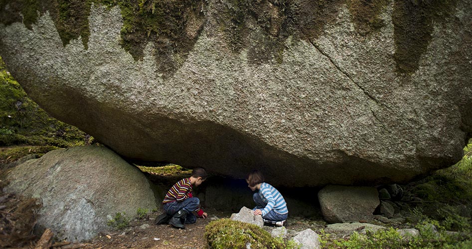 Två barn leker under ett stort klippblock i skogen.