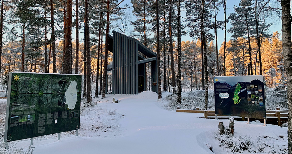 Huvudentrén En träbyggnad med skyltar framför. Det är snö på marken.