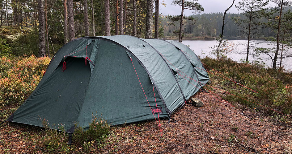 Grönt tält i skogen och en sjö i bakgrunden. 
