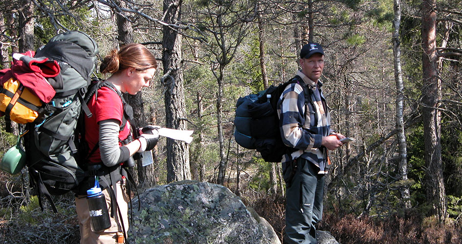 Två vandrare tittar på en karta i skogen.