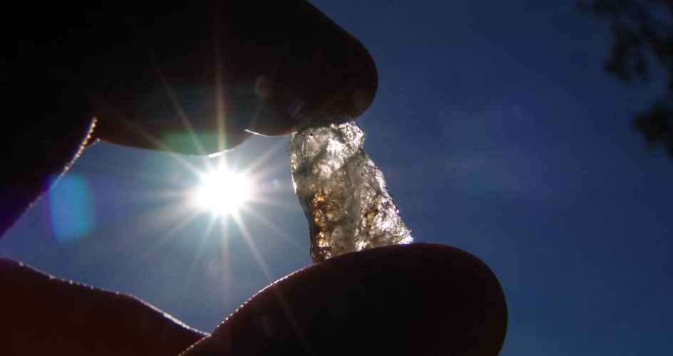 One hand holds a piece of transparent quartz against the sun.