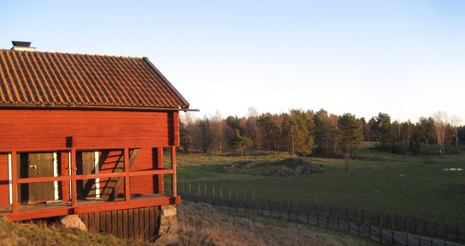 Äldre röd byggnad i solljus med öppna hagmarker i bakgrunden