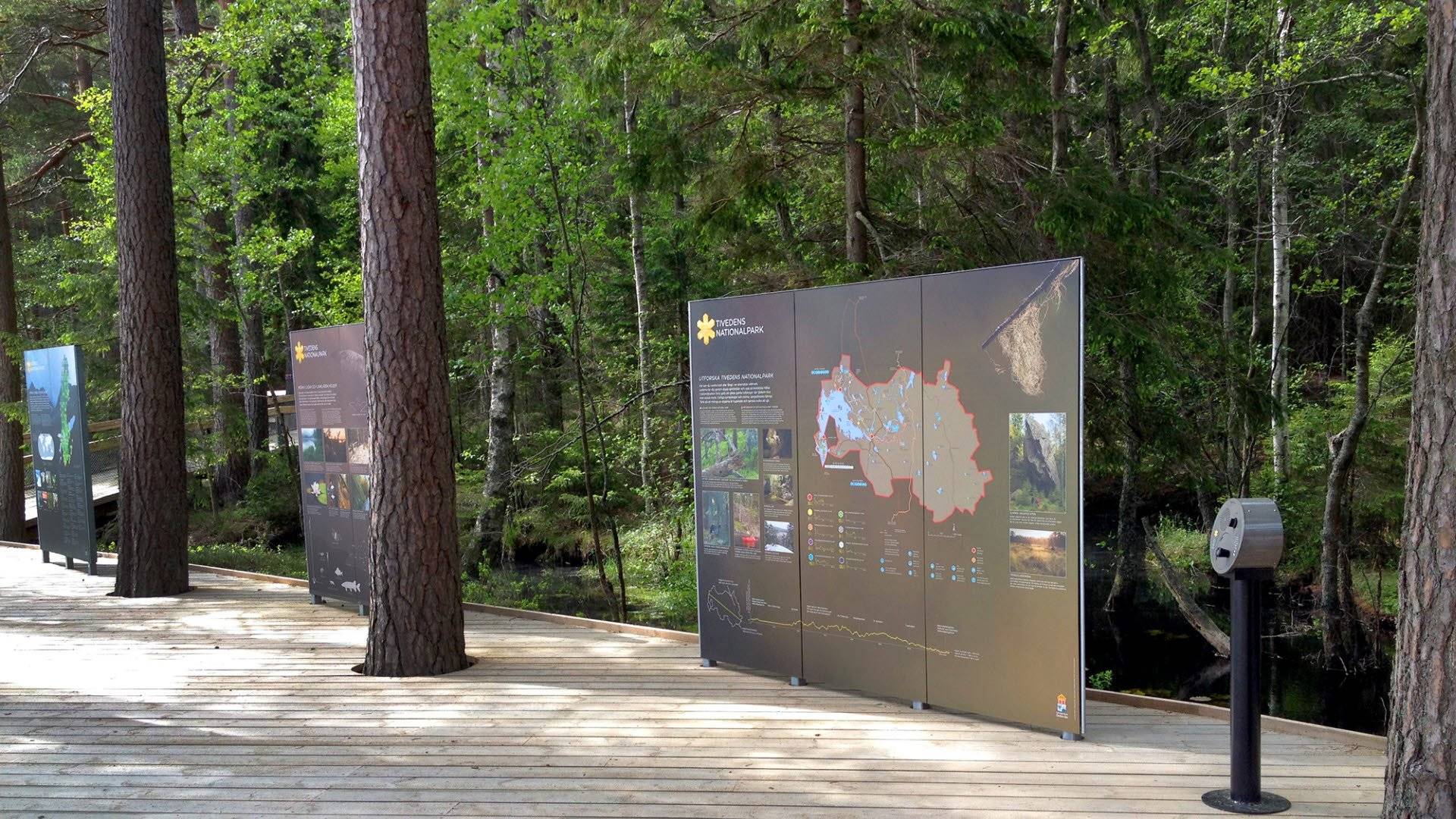 En plattform bland träd med informationsskyltar vid en av Tivedens tre entréer i Tivedens nationalpark.