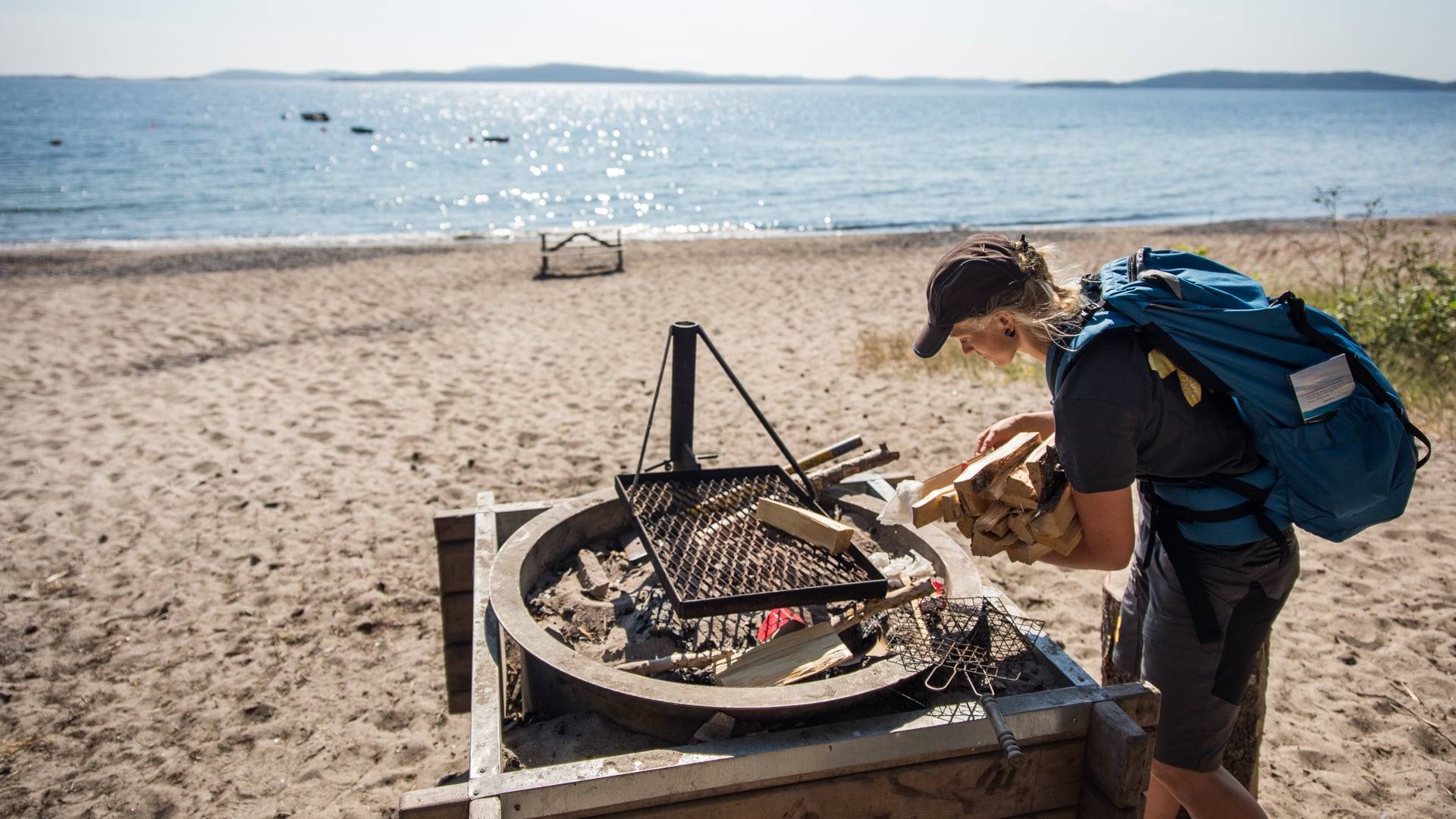 Foto av en person som bär en trave med ved vid en grillplats bredvid havet.