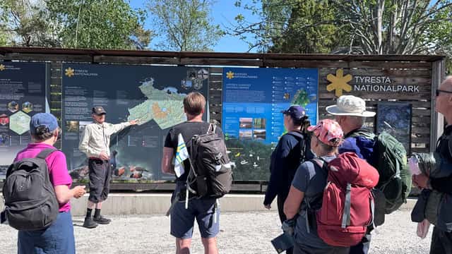 Tyresta nationalpark Flera personer med ryggsäckar står framför en informationsskylt i Tyresta nationalpark och lyssnar på en guide som pekar på kartan och berättar om nationalparken.