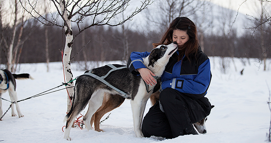 A woman is sitting with a dog in the snow.