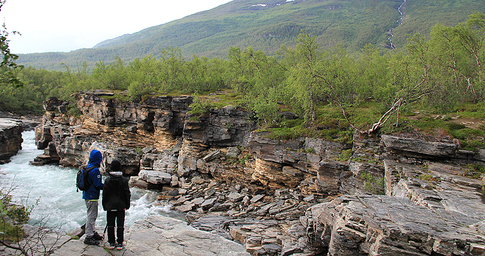 Children stand by Abisko canyon, in the background you can see a fog-covered mountain.
