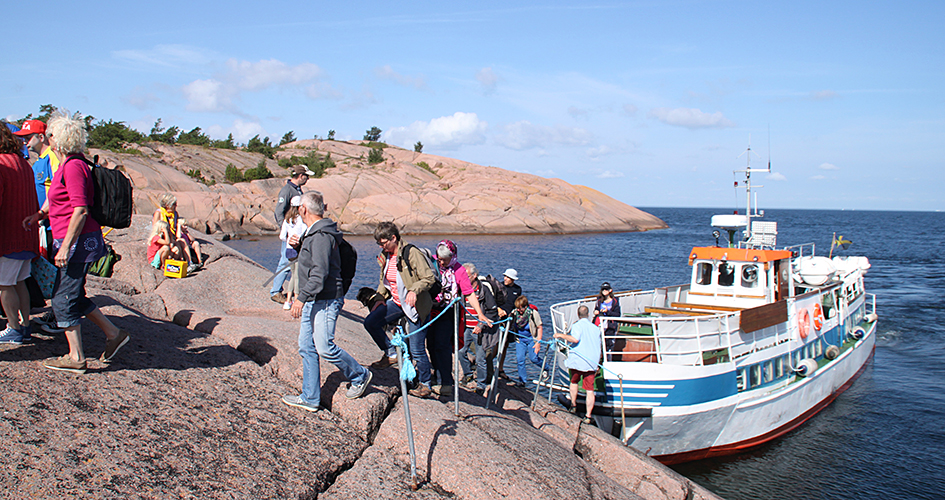 Ett led av människor som går i land på rosa klippor, från en turbåt. 