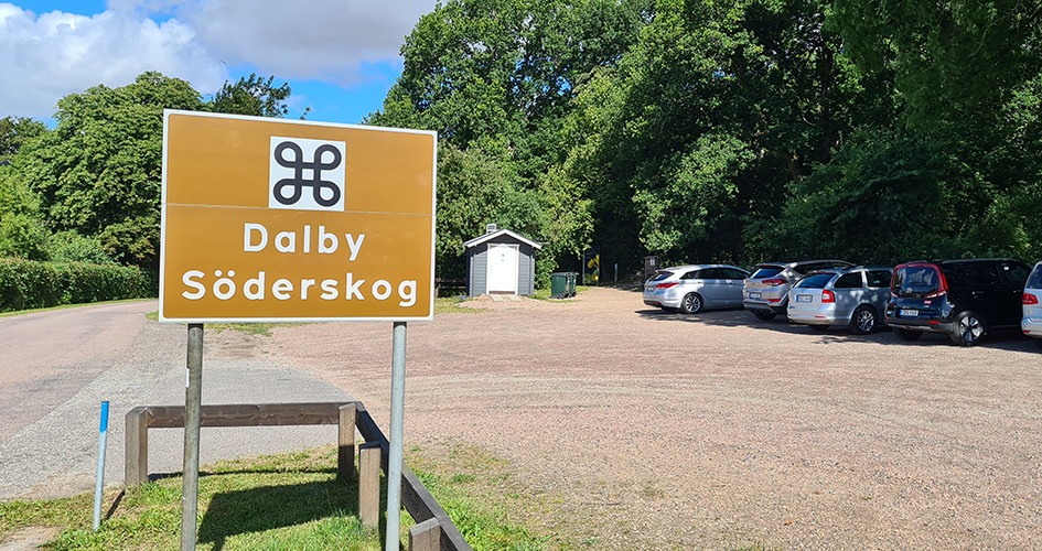 Skylt med texten Dalby Söderskog på en bilparkering med torrdass.