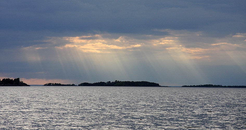 Cloudy sky, sparkling water and silhouette of island landscape.