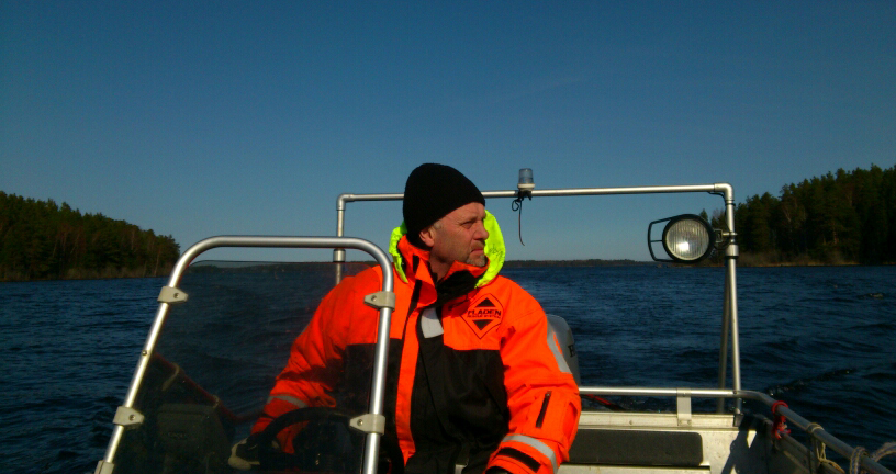 Man in orange jacket and black hat on a boat.