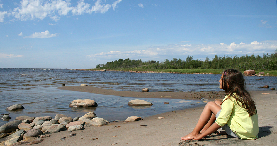 En flicka sitter på stranden och tittar ut på vattnet.