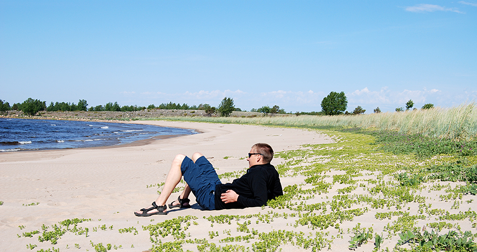 En man ligger på stranden och tittar ut över vattnet.