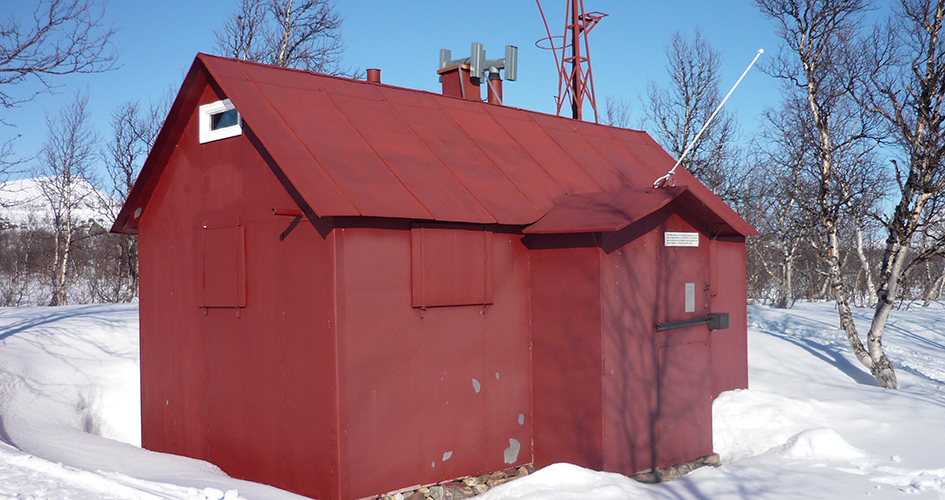 Hambergsstugai Boarek. En röd forskarstuga omgiven av snö och björkar. Himlen är klarblå.