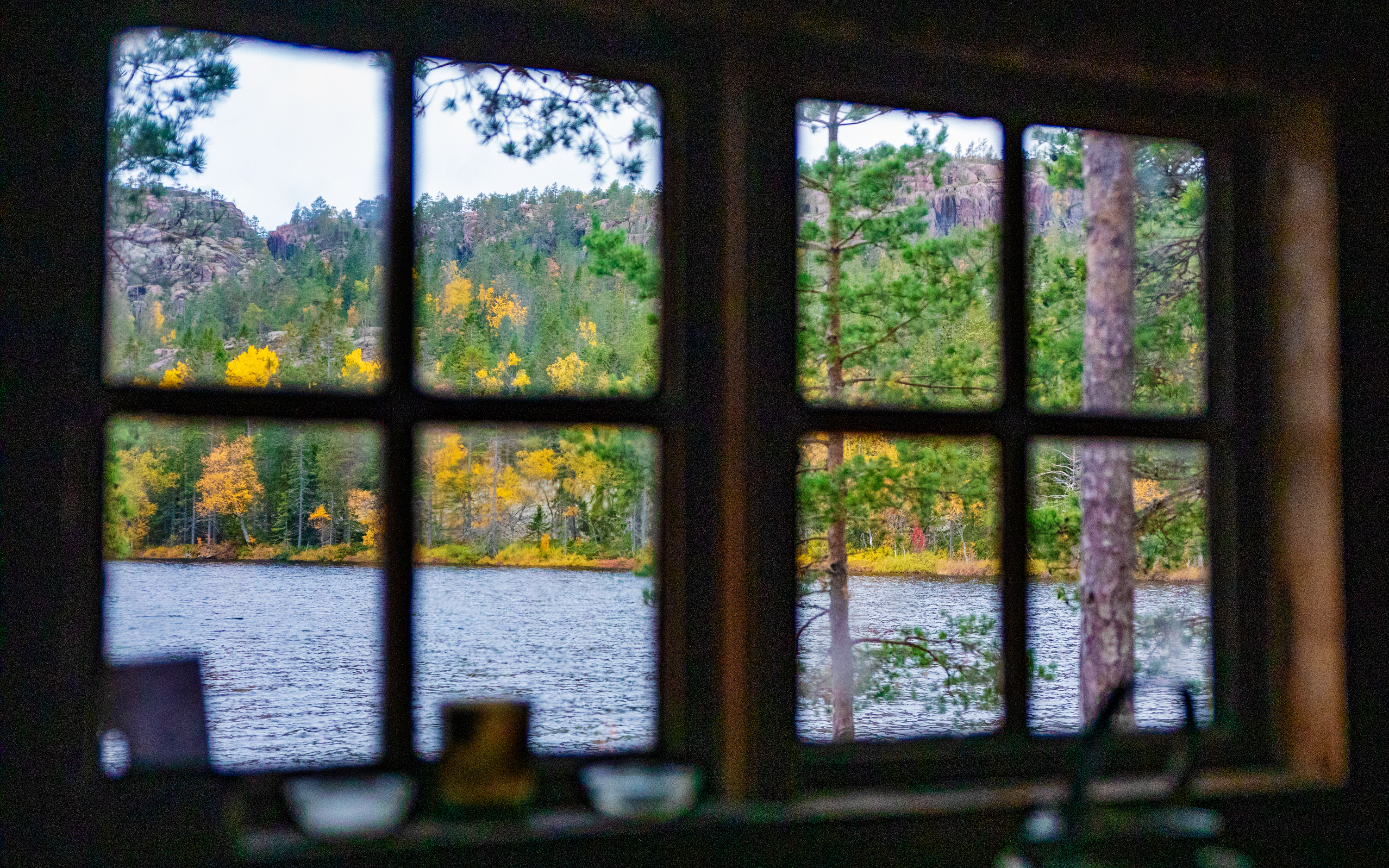 View through a window out towards a lake and a forest with autumn colors.