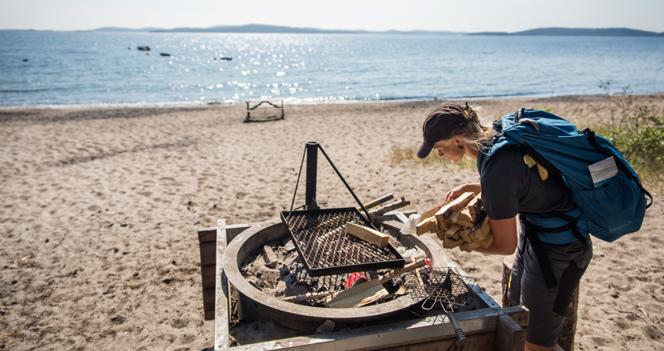 A girl holding fire wood at a fireplace at a beach.